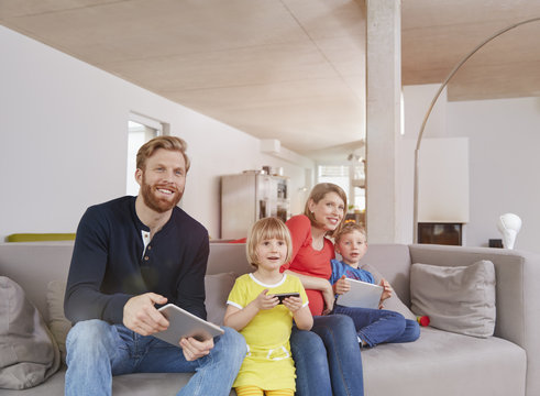 Family of four with mobile devices on couch