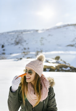Spain, Asturias, happy young woman with carrot in snowy mountains