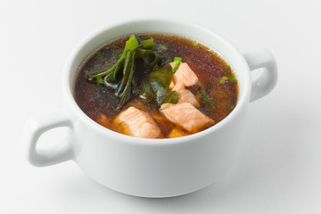 miso soup with salmon, wakame seaweed, fish broth, soy sauce and leek in white tureen on white background