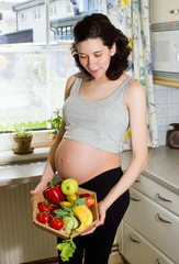 Young beautiful pregnant woman holding a basket of fruits and ve