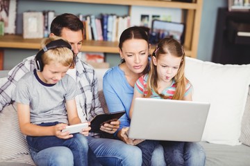 Children using technologies with parents on sofa