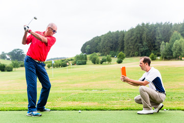 Golf trainer recording video of senior golf player