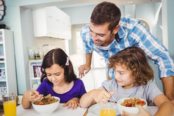 Obraz na płótnie Canvas Cheerful man with children having breakfast at home