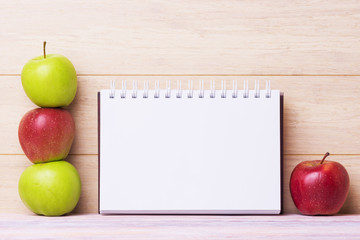 Red and green apples with note pad over wooden backgroud