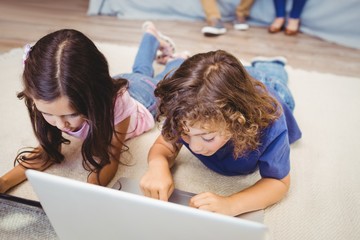 Close-up of siblings using laptop and digital tablet while lying on carpet at home