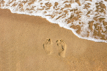 Traces of human feet on the summer beach with wave