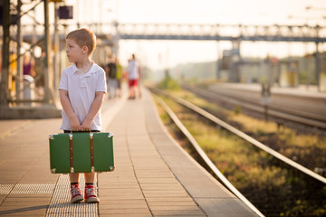 Adorable little kid boy dressed in shorts and polo t-shirt on a railway station, waiting for the...