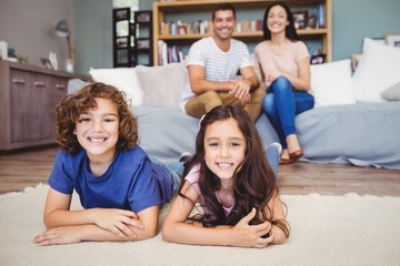 Close-up of cheerful son and daughter lying on carpet while parents sitting on sofa at home