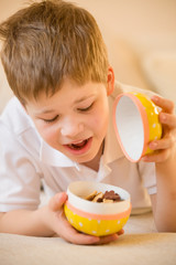 Cute boy opening a big Easter egg full of sweets and cookies. Happy kid celebrating Easter. Big yellow egg. Cheerful child with easter surprise.