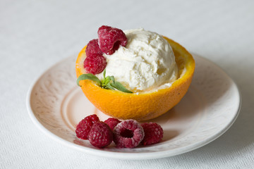 Vanilla Icecream with raspberry, summer dessert.  Delicious sundae scoop in an orange half on a white plate. Tasty sweet dessert for summer. Serving ice cream. Serving of refreshing tropical dessert
