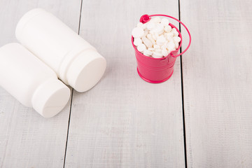 Many different white pills in a pink bucket and container