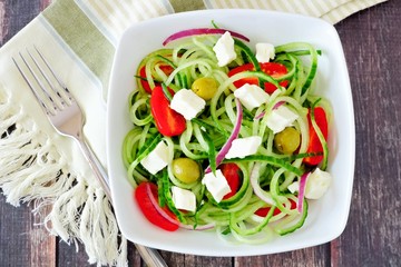 Greek Salad with cucumber noodles above scene on a dark wooden background
