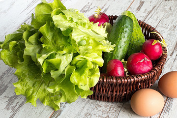 Spring vegetables.   Spring vegetables in a brown wicker basket and eggs on a light wooden background.