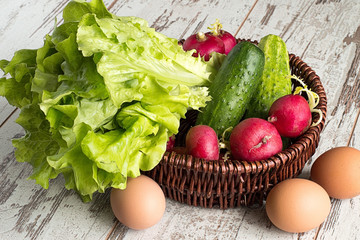 Spring vegetables.   Spring vegetables in a brown wicker basket and eggs on a light wooden background.