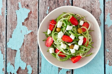 Plate of Greek Salad with cucumber noodles, overhead view on rustic wood background