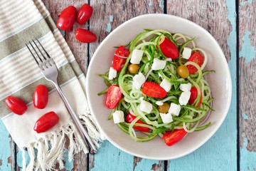 Fresh Greek Salad with cucumber noodles, overhead scene on rustic wood background