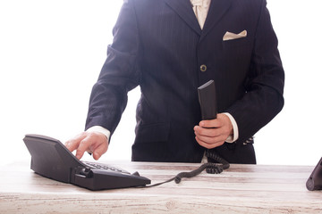 Mann am Tresen im Anzug, wählt Telefonnummer mit Telefonhörer in der Hand