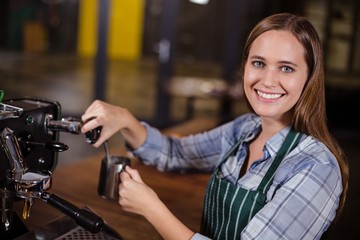 Pretty barista making hot milk with coffee machine