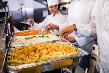 Chefs standing at serving trays of pasta 