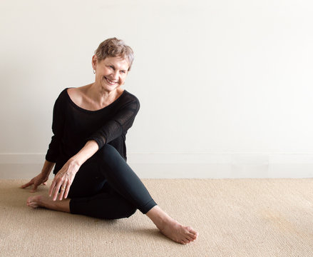 Older Woman In Black Yoga Clothing Laughing In Relaxed Seated Yoga Posture