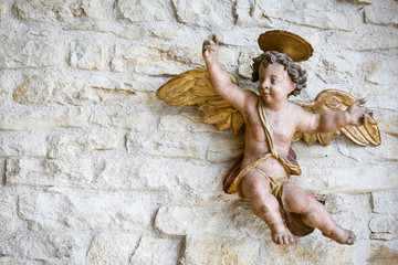Statue d'un ange en bois accroché sur un mur de pierres apparentes