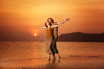Fototapeta premium Couple of happy young lovers raising hands at golden sunset