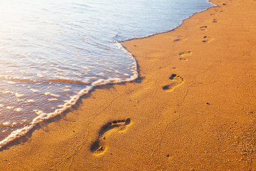 beach, wave and footprints at sunset time