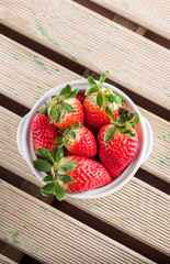 strawberries group in white ceramic bowl on rustic wooden table