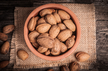 Tasty almond nuts in clay bowl on rustic wooden background