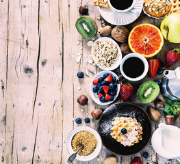Obraz na płótnie Canvas Health and colorful breakfast - cups of coffee with oat flakes, waffles, muffins,almond,hazelnuts,various fruits, berries and milk on old wooden table. Health food concept .Top view.