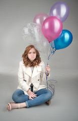 Fototapeta na wymiar Sad young adult sitting on floor holding balloons