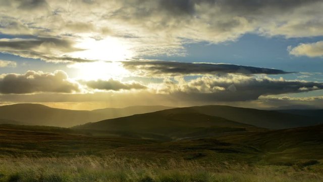 Sunbeams breaking through clouds, mountain scenery as a backdrop. Time lapse, zoom in, pan left.