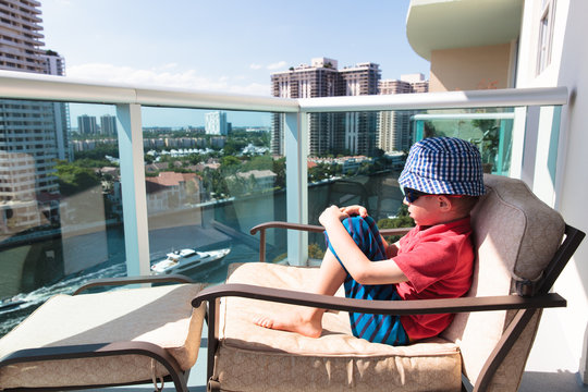 little boy relax on the balcony of hotel looking at cityscape