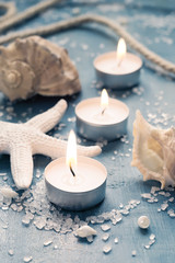 Fototapeta na wymiar Three burning candles in a row on background of sea objects, tin