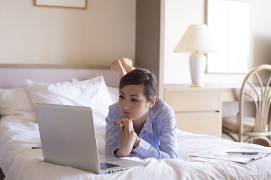 Woman is using a laptop lying face down in bed