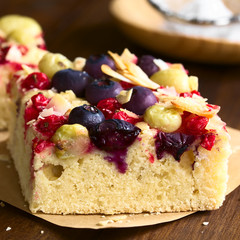 Homemade cake with gooseberry, blueberry, redcurrant and coconut flakes, photographed on dark wood with natural light (Selective Focus, Focus on the front of the cake dough and some berries)