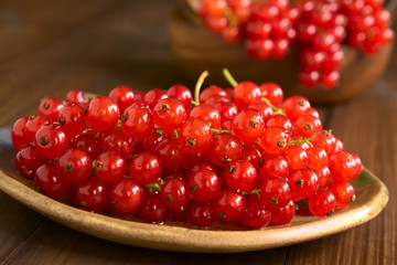 Raw red currants (lat. Ribes rubrum) on plate, photographed on dark wood with natural light (Selective Focus, Focus one third into the redcurrants)
