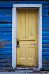 Weathered yellow door inset in faded and peeling exterior wood board wall