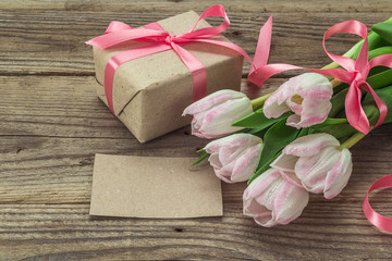 Blank card, pink tulips and gift box on a  grunge wooden backgro