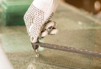 Closeup hand wearing white work gloves using metal cutting tool on transparent piece of glass