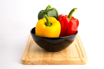 Sweet peppers in ceramic bowl and wood block on white back groun