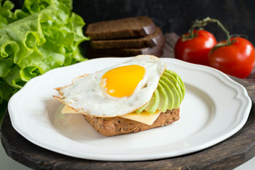 Fried egg, avocado and cheese on toasted bread. Healthy breakfast on a plate
