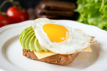 Sunny side up egg, avocado and cheese on whole grain toast for healthy breakfast