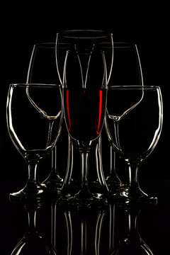 Red water in wine glass and empty glasses on black background