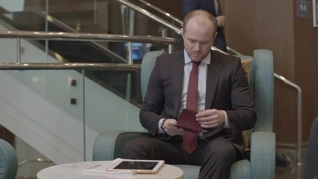 Businessman sitting in the hotel lobby, checking time and airplane tickets and using his digital tablet