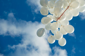 White balloons fly up into the blue sky. The release of festive balloons in the clouds. Celebration and happiness. Air gel balls in the atmosphere.