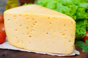 Tilsit Tilsiter cheese of the semi-hard cheese with vegetables on a wooden background