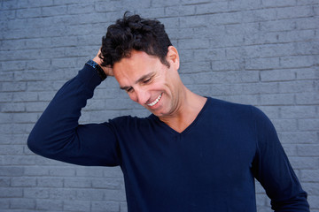 Handsome man laughing with hand in hair against gray wall