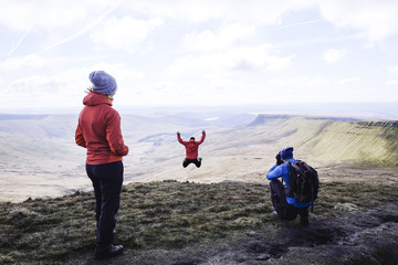 Fototapeta A group on top of a mountain, with a photographer and a girl jumping, Pen Y Fan obraz