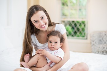 Smiling mother carrying daughter while sitting on bed at home 